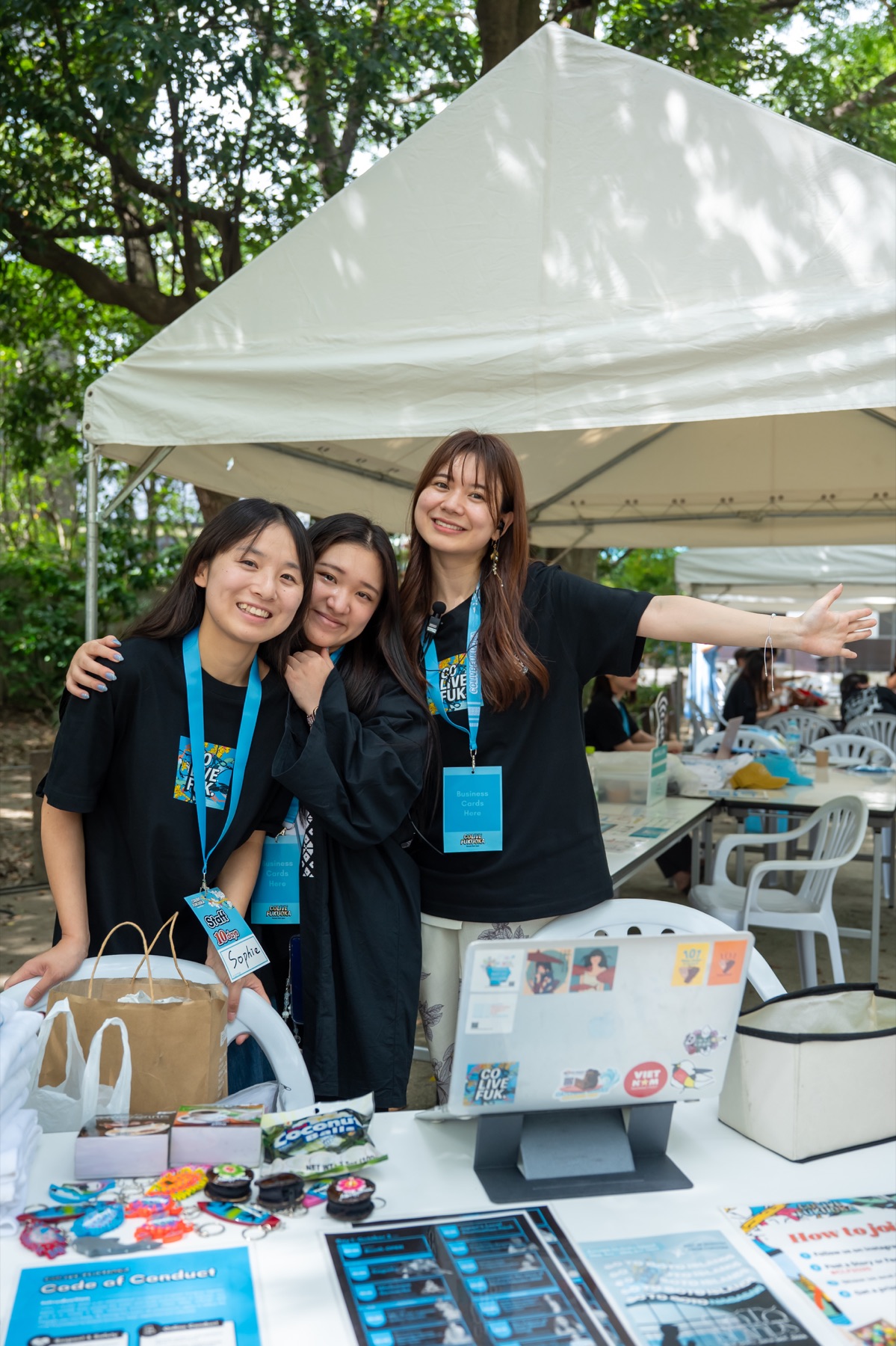 Three smiling Colive Fukuoka volunteers at the 2025 welcome desk